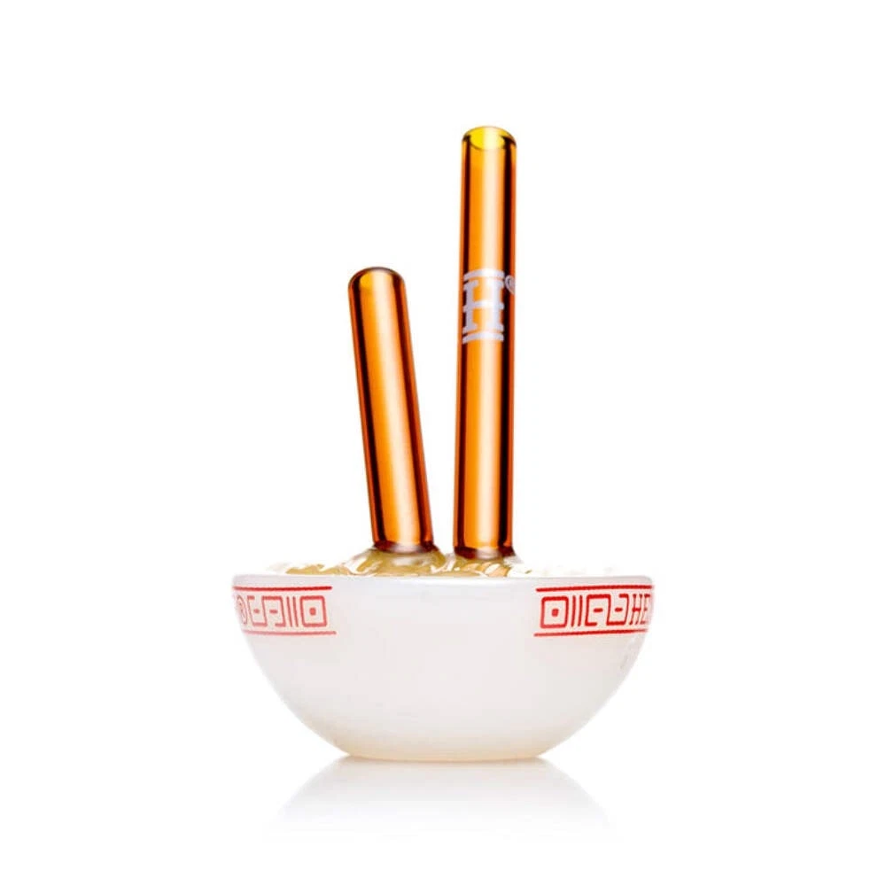 Two amber glass vape pens standing upright in a small white ceramic bowl with red decorative patterns, on a clean white background.