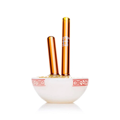 Two amber glass vape pens standing upright in a small white ceramic bowl with red decorative patterns, on a clean white background.